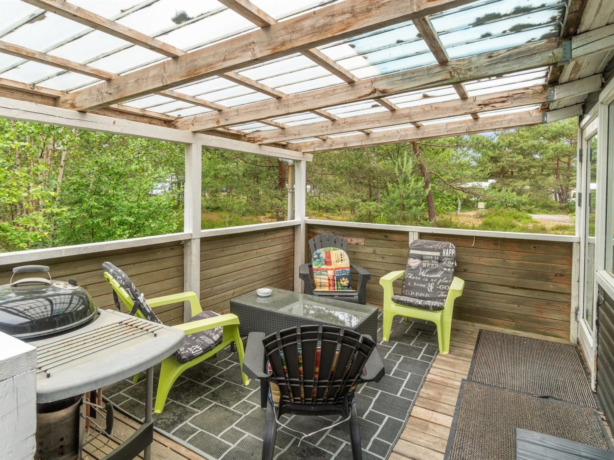 Eine überdachte Terrasse mit Grill, Stühlen und Tisch.