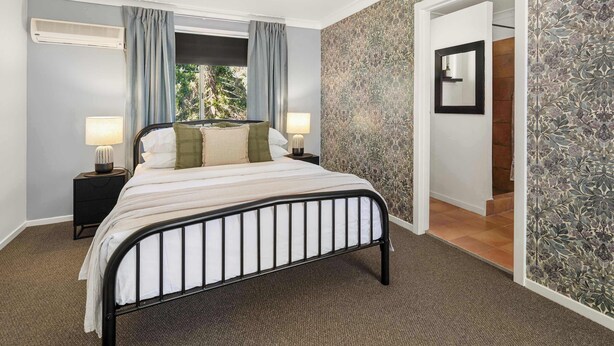 Une chambre à coucher avec un lit, deux tables de chevet avec des lampes, une fenêtre avec des rideaux et un mur à motifs.