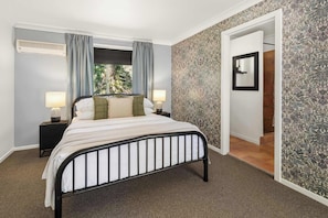 A bedroom with a bed, two bedside tables with lamps, a window with curtains, and a patterned wall.