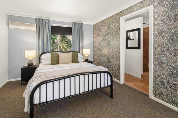 A bedroom with a bed, two bedside tables with lamps, a window with curtains, and a patterned wall.