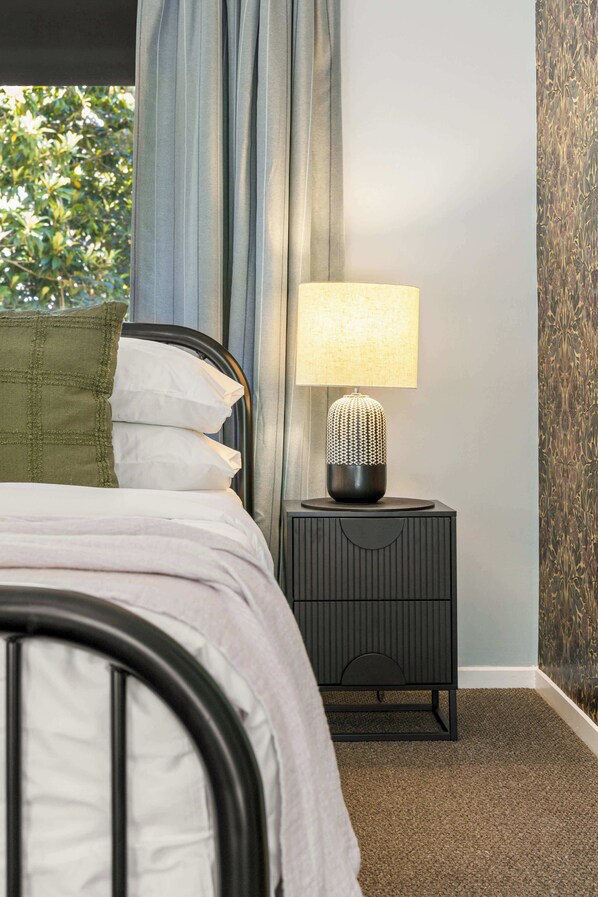 A bedroom with a bed, a nightstand with a lamp, and a window with curtains.