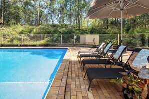 A swimming pool with lounge chairs and an umbrella.