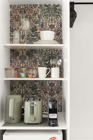 A kitchen with a white shelf holding a coffee maker, a toaster, and a kettle.