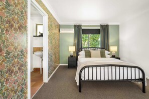 A bedroom with a bed, nightstands, a lamp, a window with curtains, and a bathroom with a sink and mirror.
