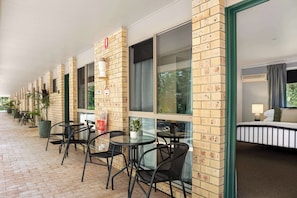 A hotel corridor with brick walls, large windows, and outdoor seating with chairs and tables.