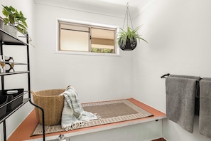 A bathroom with a window, a hanging plant, a shelf with toiletries, and a towel rack.