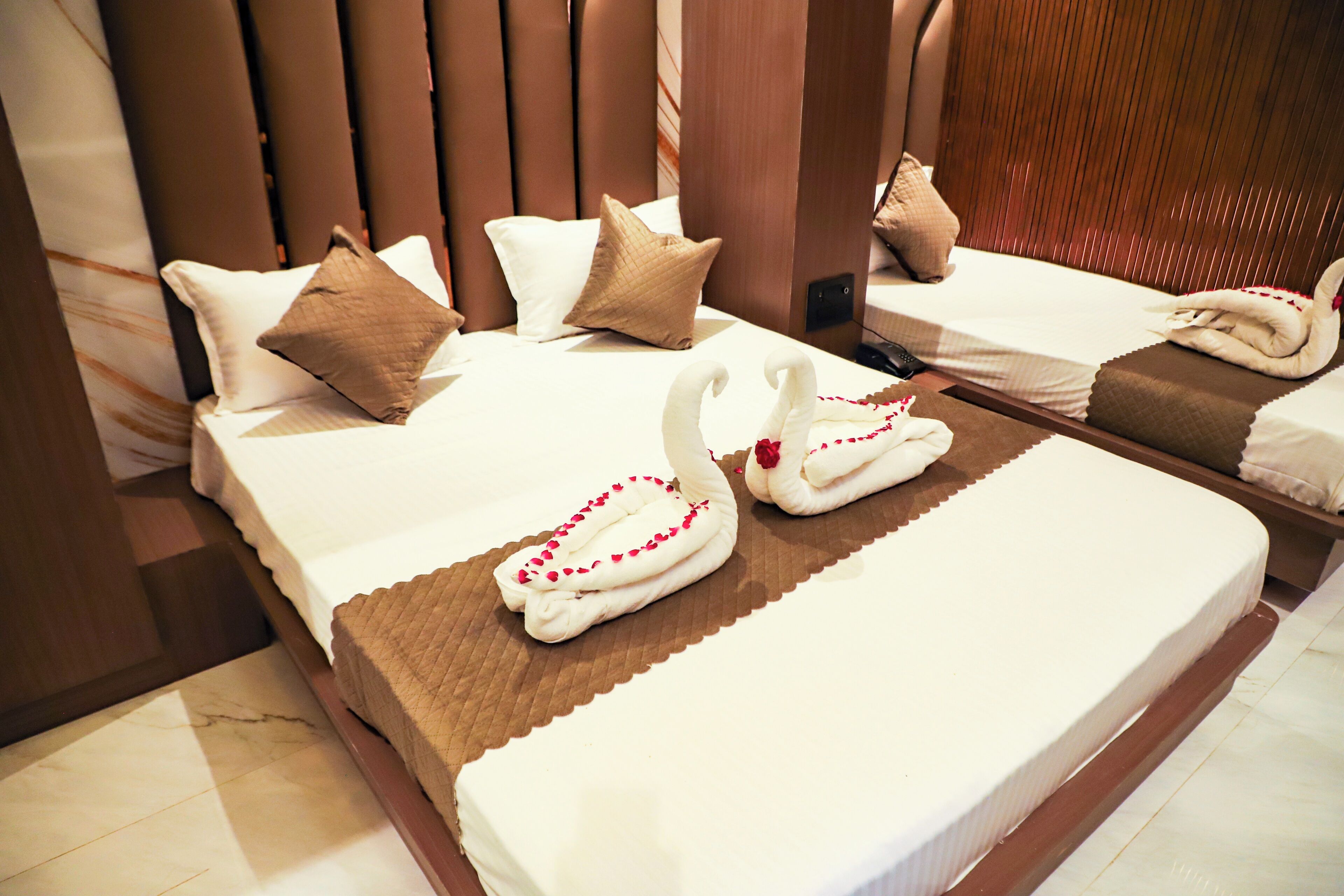 A hotel room with two beds, each with a brown headboard, white bedding, and decorative swans made of towels.