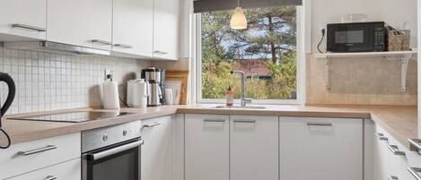 A modern kitchen with white cabinets, a built-in oven, a microwave, and a window with a view of trees.