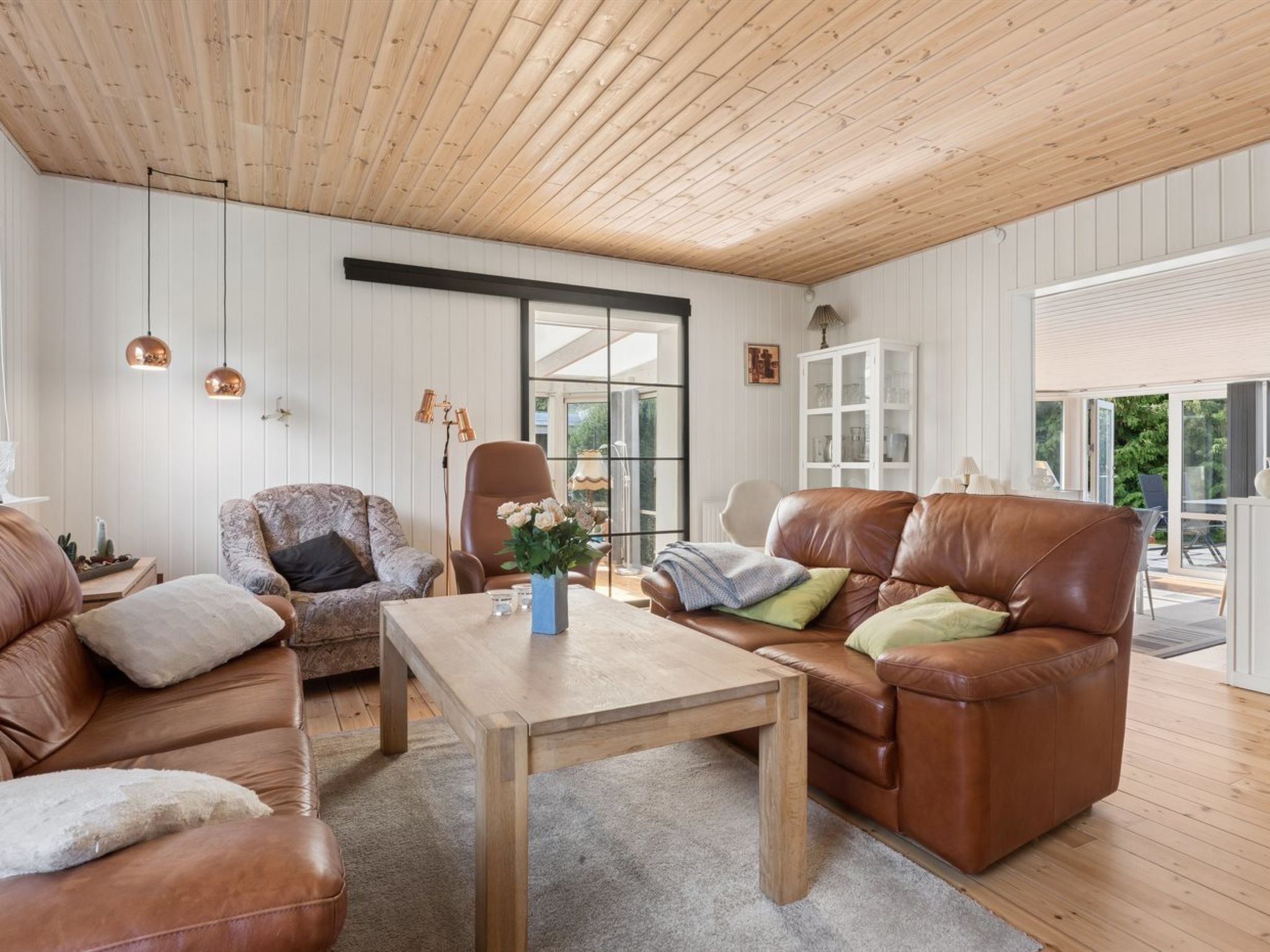 Un salon spacieux avec un plafond haut, des canapés en cuir, une table basse en bois et des luminaires suspendus.