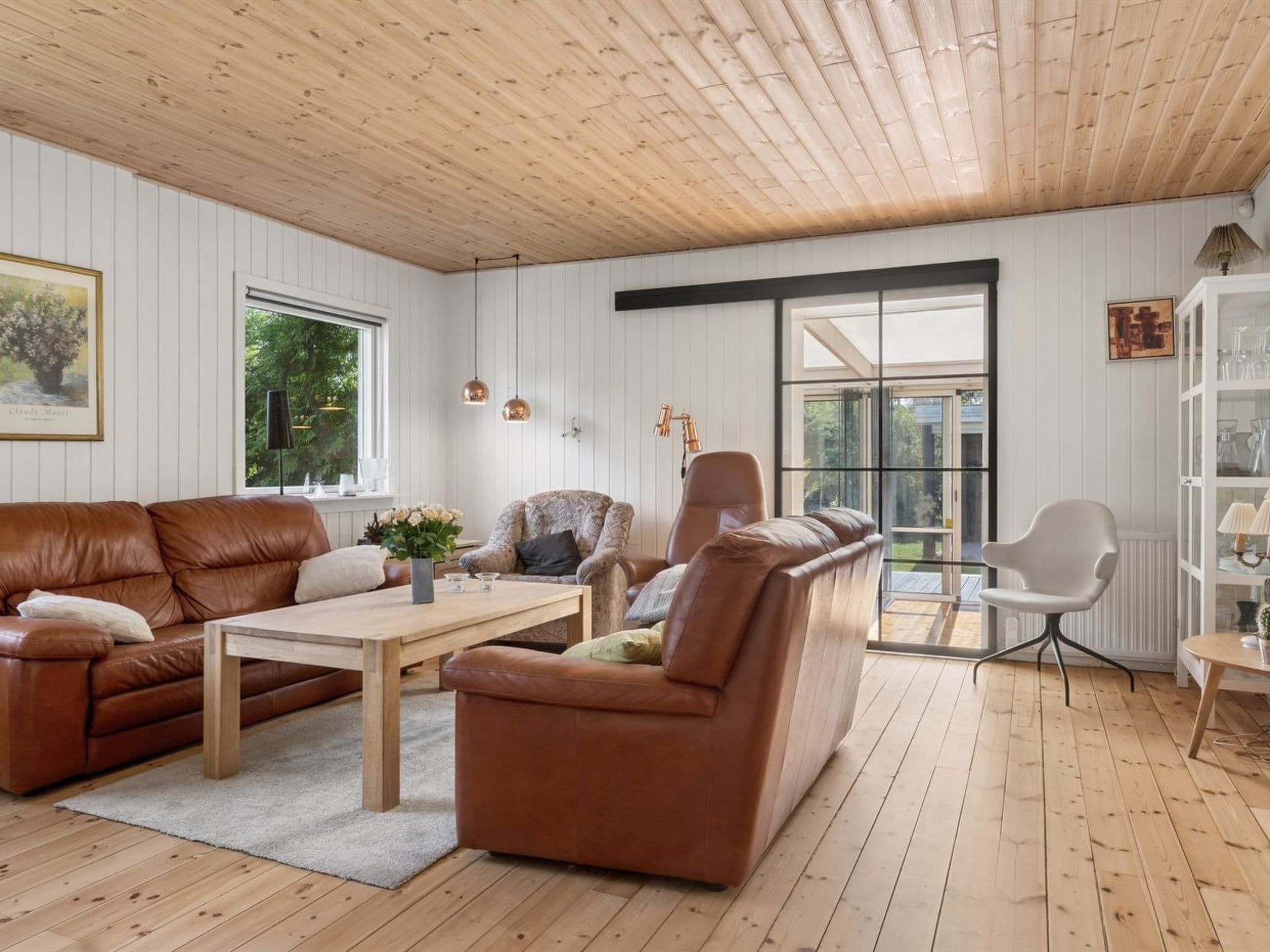 A spacious living room with a wooden ceiling, leather sofas, a coffee table, and a glass cabinet.