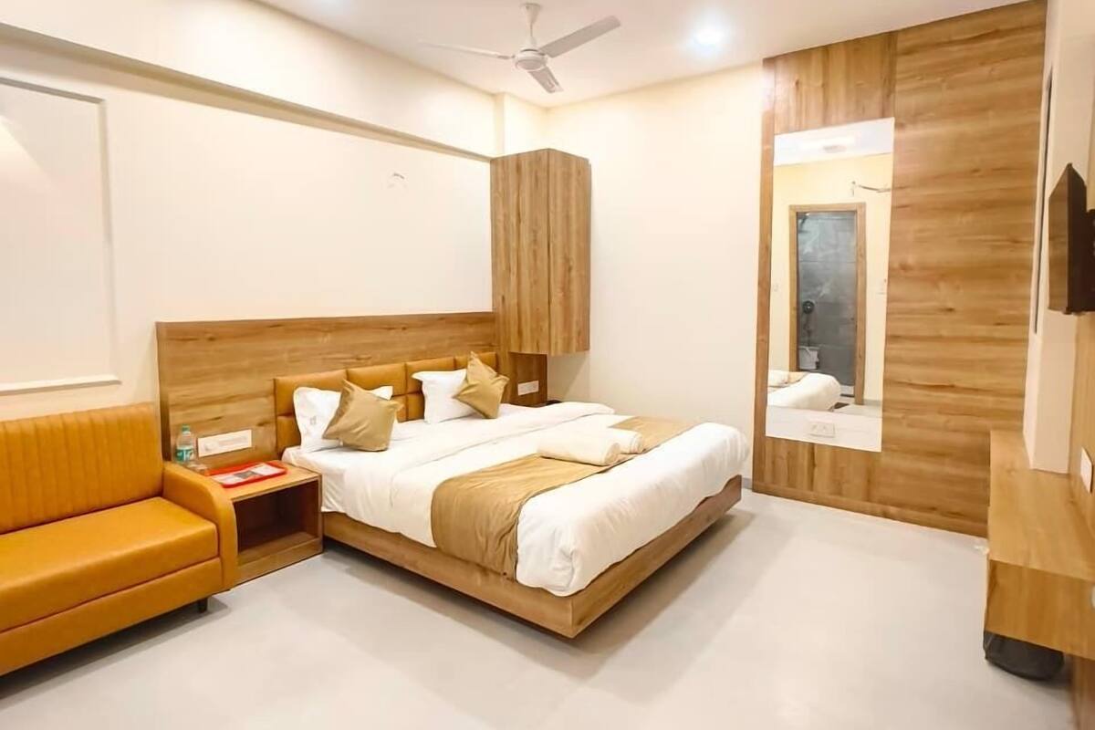Un dormitorio moderno con cabecera de madera, cama con ropa de cama blanca, mesita de noche de madera, sofá y ventilador de techo.
