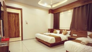 A hotel room with two beds, a wooden wardrobe, a desk, and a modern ceiling light fixture. - Hotel Vistara (Ujjain)