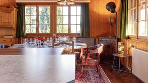 Una cabaña de madera con comedor que cuenta con una isla de mármol, un candelabro y vistas al bosque a través de amplios ventanales.