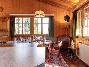 Eine Holzhütte mit Essbereich, ausgestattet mit einer Marmorinsel, einem Kronleuchter und Blick auf den Wald durch große Fenster.
