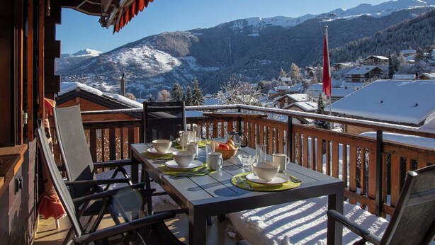 Una terraza de madera con una mesa lista para cenar, con vistas a un paisaje montañoso nevado.