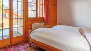 Un dormitorio con una cama de madera, un radiador, una ventana con cortina y vistas a un edificio.