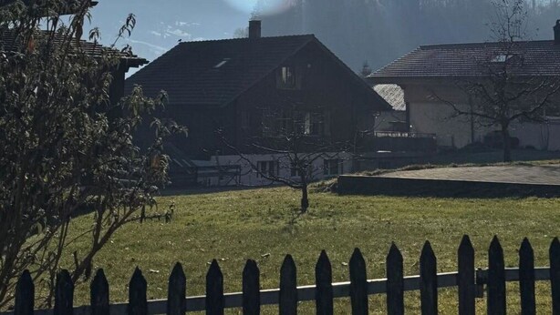 Maaseutumaisema, jossa on talo, aita ja taustalla näkyvät vuoret.