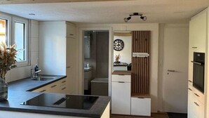 Moderni keittiö, jossa on keskeinen saareke, puupalkit katossa ja näkymä olohuoneeseen.