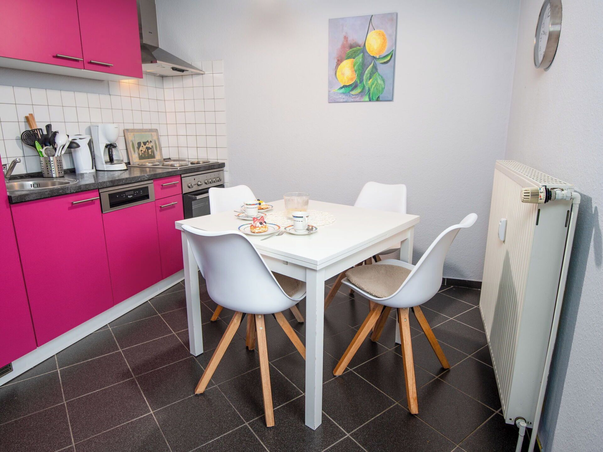 Una cocina compacta con una mesa blanca, dos sillas y un radiador.