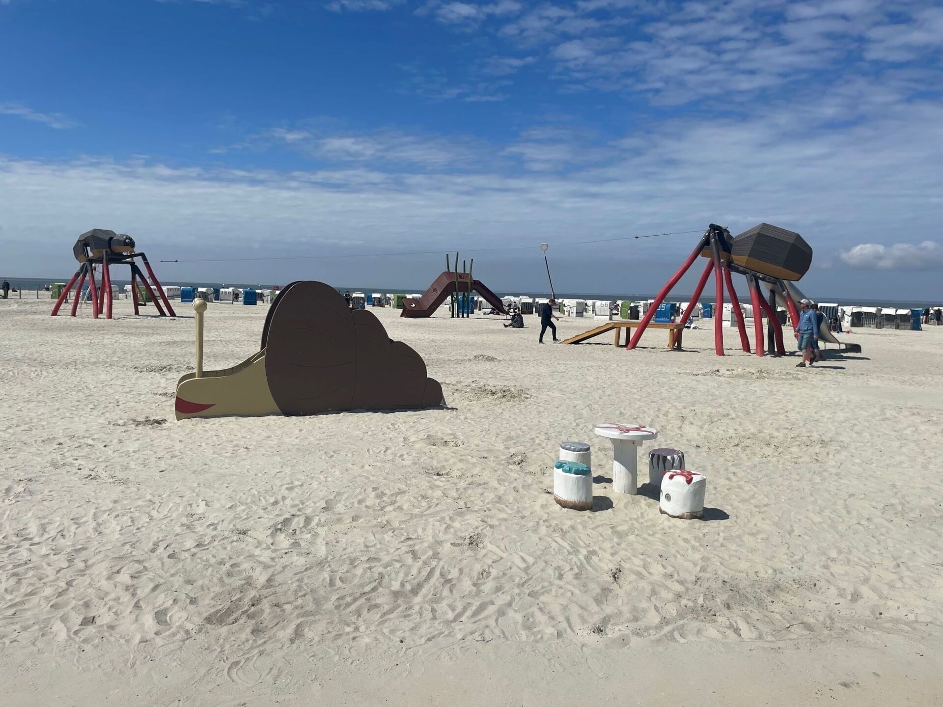 Une plage de sable où se dressent de grandes sculptures abstraites et quelques conteneurs blancs.