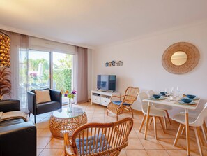 Ein modernes Wohnzimmer mit Sofa, Esstisch, Stühlen, einem Fernseher und einem Balkon mit Pflanzen.