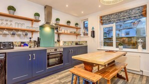 Une cuisine moderne avec des meubles bleus, une table en bois et une fenêtre donnant sur une maison.