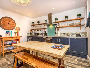Eine kleine Küche mit Holztisch, integrierten Geräten und einer Wanduhr.