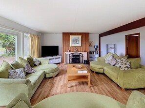 Ein Wohnzimmer mit zwei grünen Sofas, einem Flachbildfernseher, einem Kamin und einem Holztisch.
