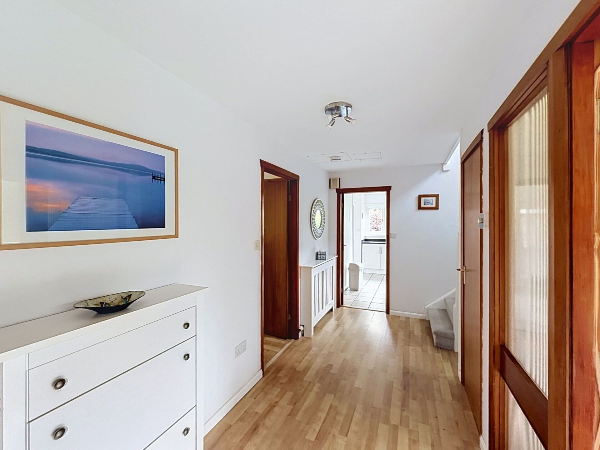 Un pasillo con piso de madera, un aparador blanco, un cuadro en la pared y una puerta que da a otra habitación.