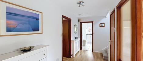Un pasillo con piso de madera, un aparador blanco, un cuadro en la pared y una puerta que da a otra habitación.