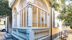 Ein Gebäude mit großen Bogenfenstern, einem Balkon mit Brüstung und einer kleinen Außen-Sitzgelegenheit.