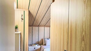 Ein gemütliches Schlafzimmer mit einem Holzschrank, einem Nachttisch mit Pflanze und einem Bett mit gesteppter Bettdecke.