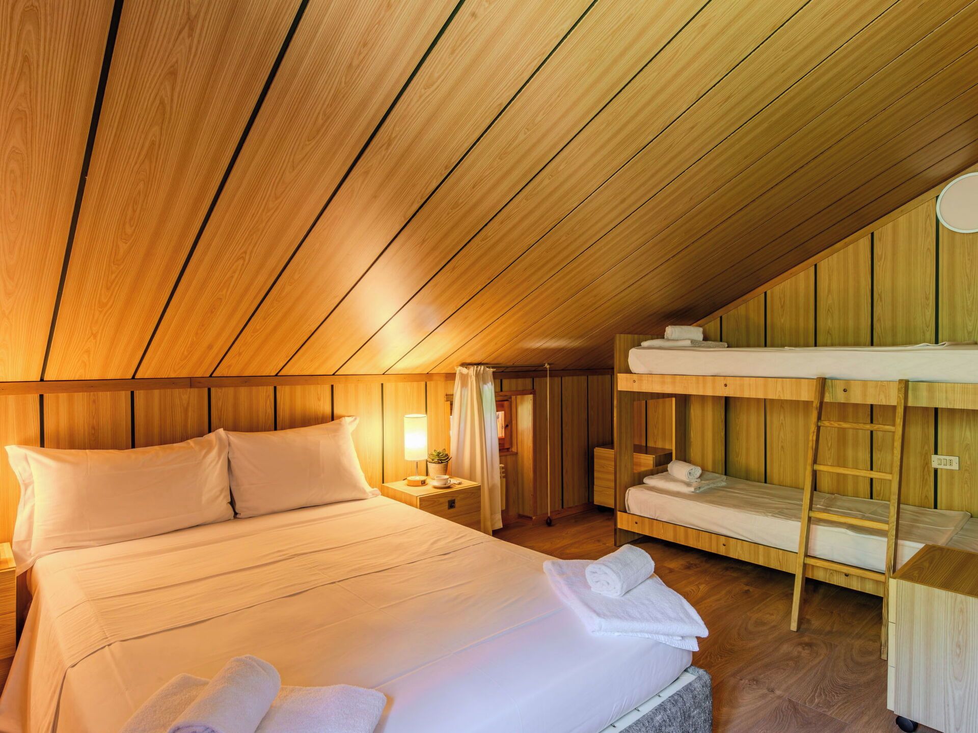 Ein gemütliches Schlafzimmer im Dachgeschoss mit einem großen Bett, einem Etagenbett, Holzwänden und einer geneigten Decke.