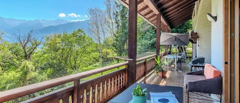 A balcony with a view of mountains, a table with a plant, and outdoor furniture.