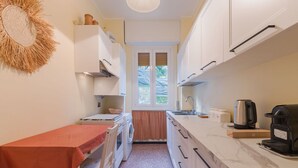 Une cuisine compacte avec des meubles blancs, un four encastré, un évier et une machine à café.