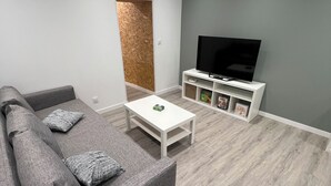 A modern living room with a grey sofa, a white coffee table, and a flat-screen TV on a white stand. - Maison des Volcans - 3 double bedrooms - 2 bathrooms - Patio - Wifi (Ceyrat)