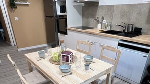 A modern kitchen with a wooden dining table, chairs, and a built-in oven. - Maison des Volcans - 3 double bedrooms - 2 bathrooms - Patio - Wifi (Ceyrat)