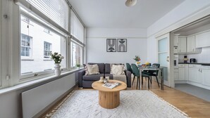 Un salon moderne avec un canapé, une table basse et un coin repas. On aperçoit une cuisine à l’arrière-plan.