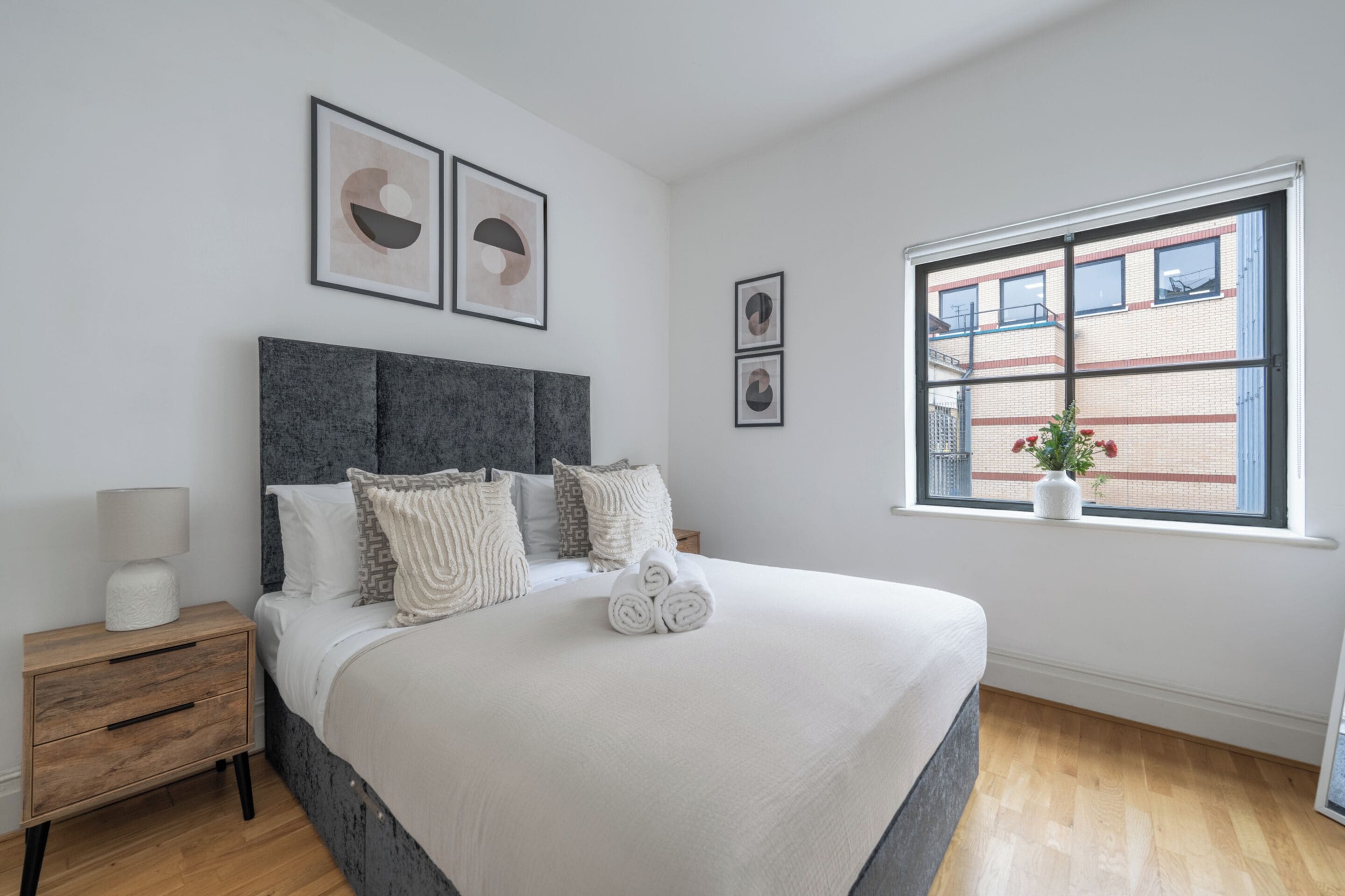A neatly arranged bedroom with a bed, bedside table, and a window with a view of a building.