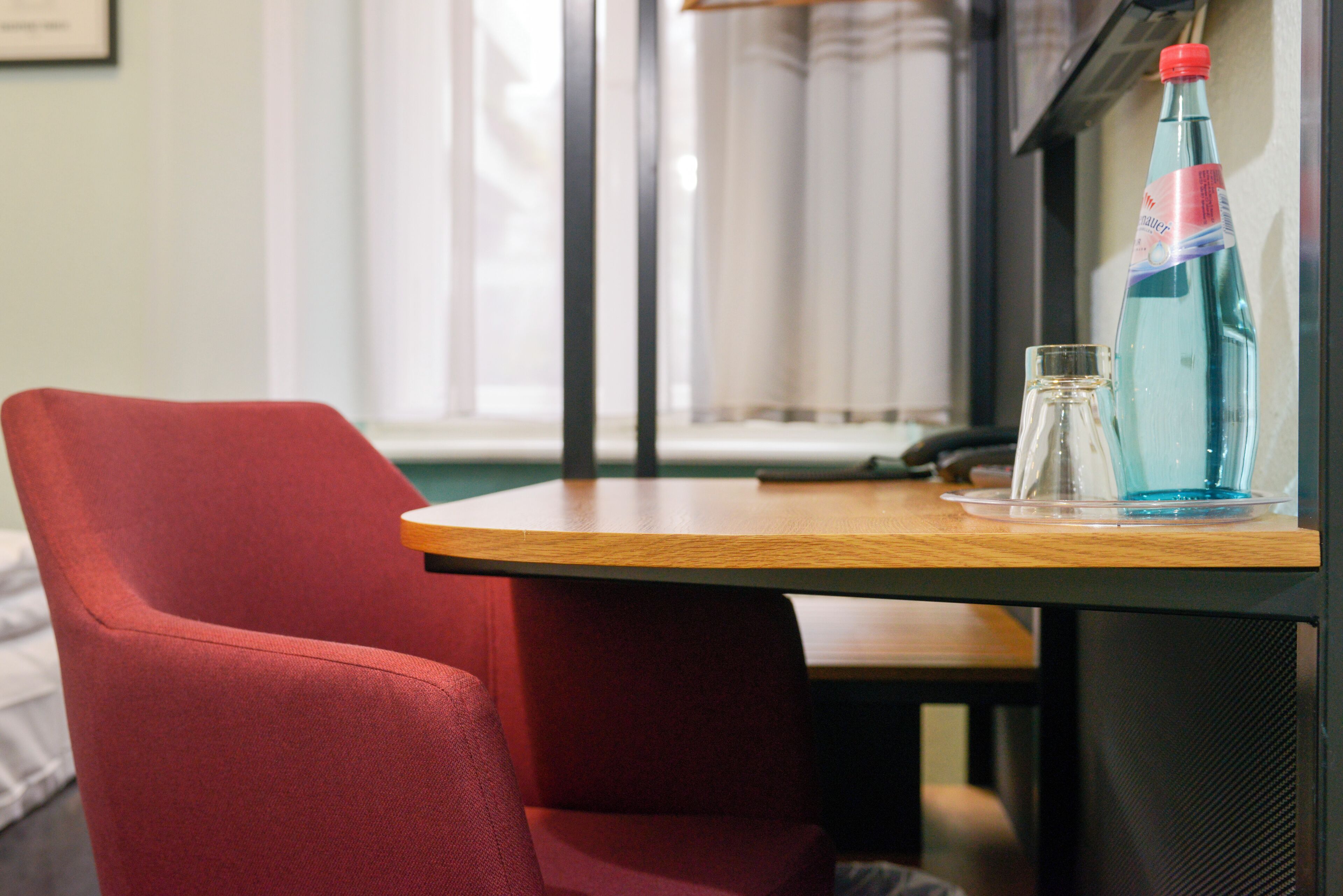 A hotel room with a wooden table, a red chair, and a bottle of water on the table.