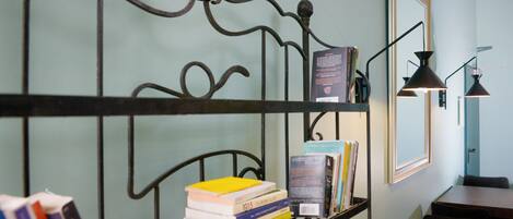 Una habitación con estructura metálica para la cama, una estantería con libros, un espejo y un escritorio con lámpara.