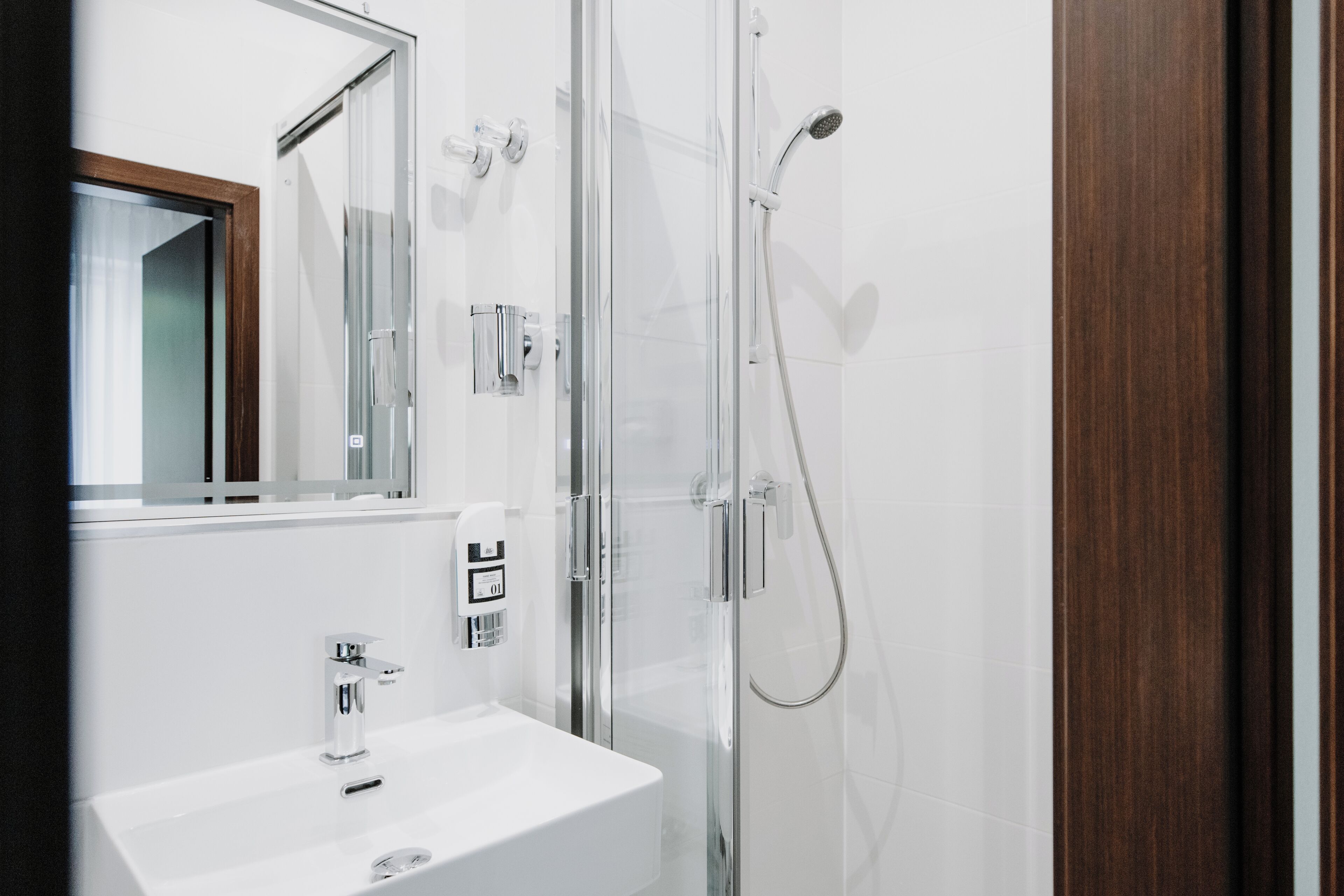 A modern bathroom with a glass-enclosed shower, a white sink, and a mirror with a wooden frame.