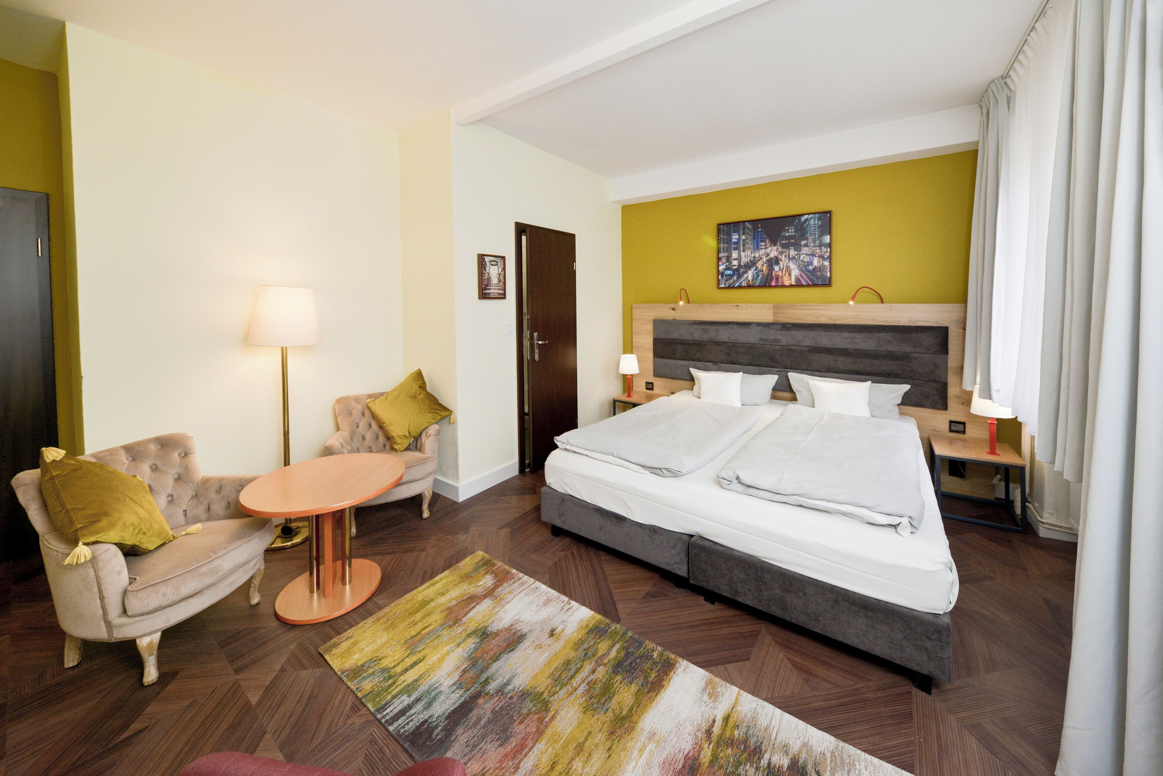 A hotel room with a bed, a sofa, a small table, and a lamp.
