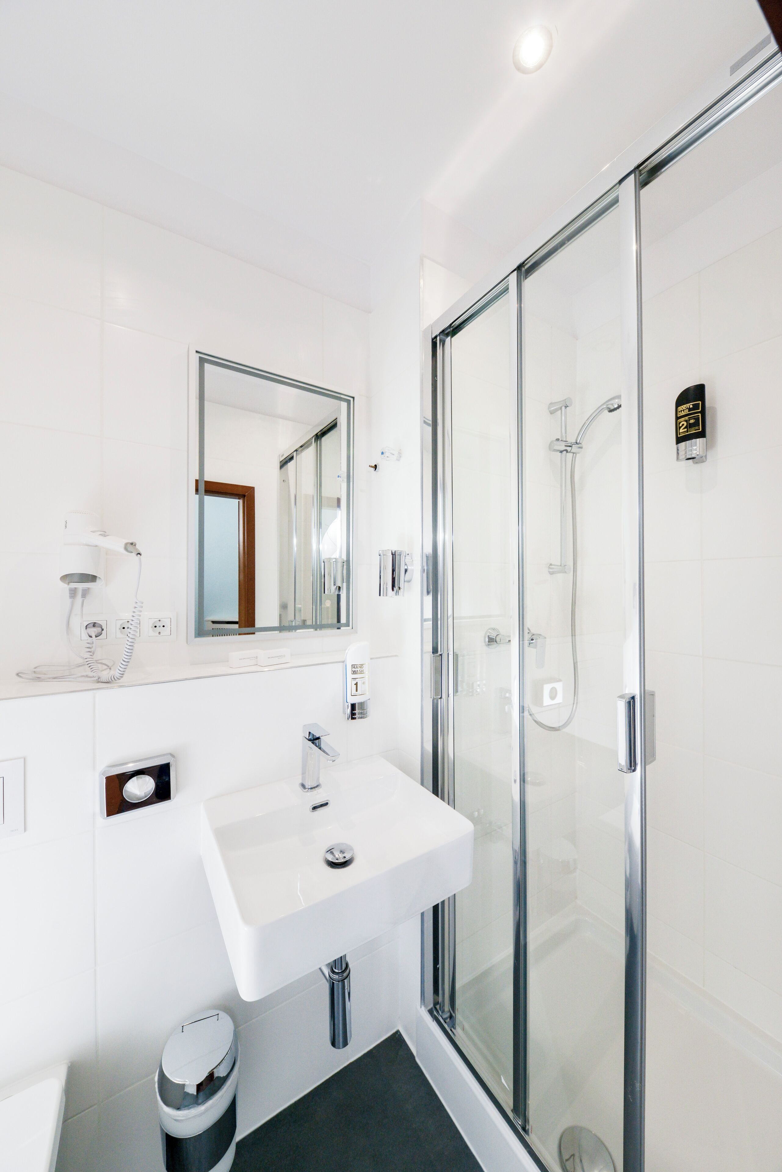 A modern bathroom with a glass-enclosed shower, a white sink, and a mirror above it.