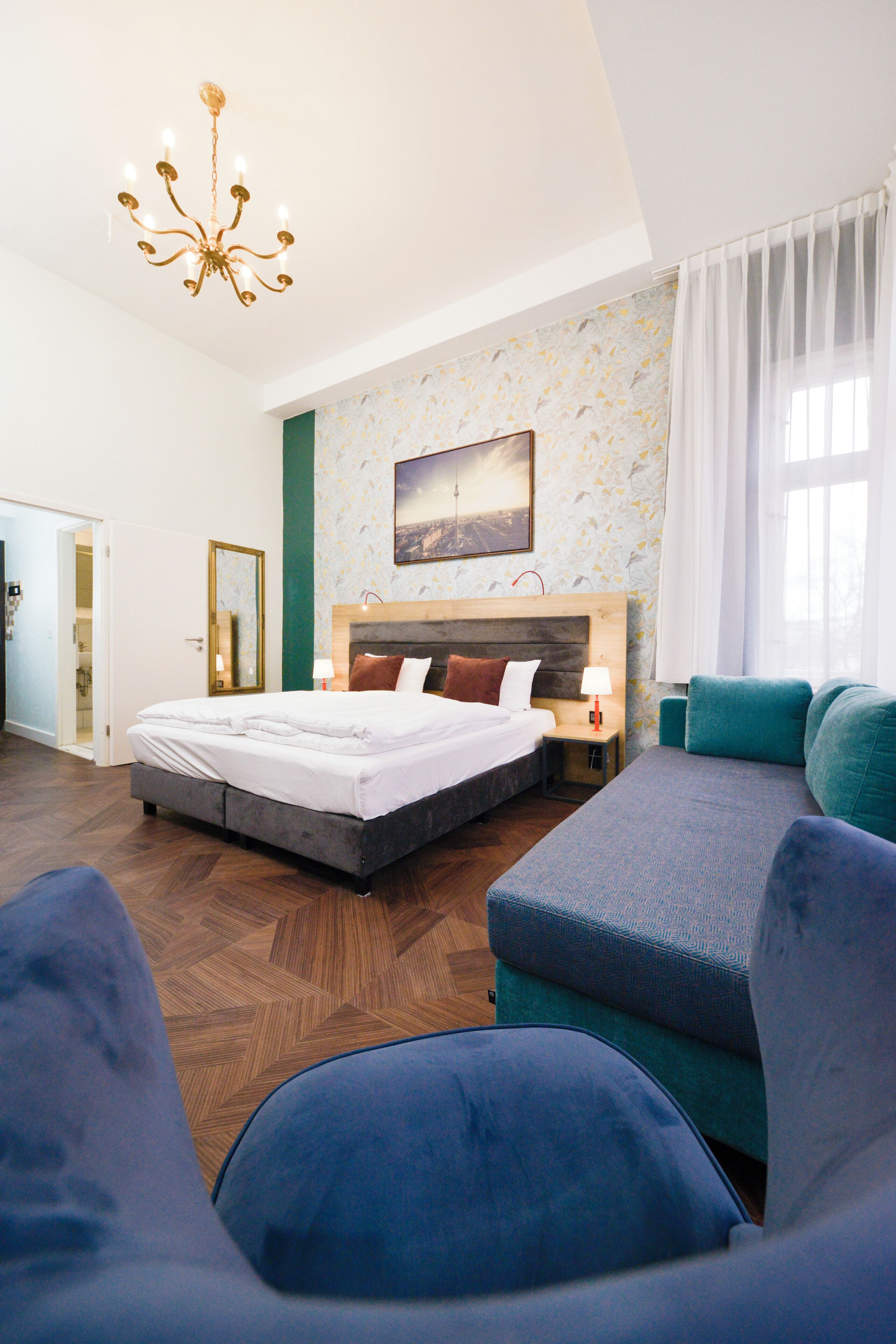 A modern hotel room with a large bed, a sofa, a chandelier, and a painting on the wall.