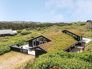 Ein modernes Gebäude mit Gründach, umgeben von einer natürlichen Landschaft und Blick auf das Meer.