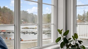 Ein Zimmer mit großen Fenstern und Blick auf einen Hafenbereich mit Booten und einer bewaldeten Landschaft.