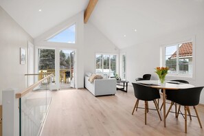 En rummelig opholdsstue med højt til loftet, store vinduer og en balkon med udsigt over landskabet.