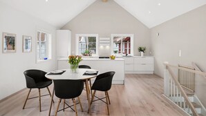Eine moderne Küche mit weißen Schränken, ein Essbereich mit rundem Tisch und schwarzen Stühlen sowie eine Treppe mit Holzbalken.