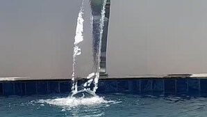 Una piscina con una fuente de agua cristalina y un borde de piedra.